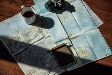 Draufsicht auf eine alte Fotokamera und einen Metallbecher mit Kaffee auf einer Straßenkarte während einer Reise - ADSF25921