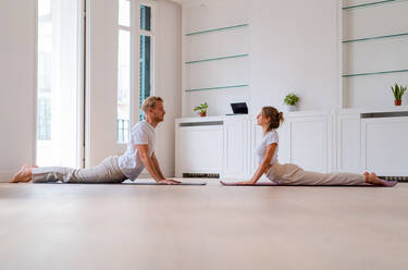 Lying on yoga mat young woman holding muscular man on lifting legs