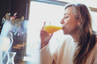 Zufriedene Frau mit einem Glas Orangensaft am Tisch sitzend beim Frühstück - ADSF25970