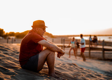 Seitenansicht in voller Länge kontemplativen erwachsenen Mann in Sommerkleidung Ruhe auf warmen Sandstrand bei Sonnenuntergang - ADSF25981