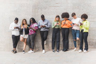 Gruppe junger multiethnischer Partner in Freizeitkleidung surfen im Internet auf Handys auf einem Gehweg in der Tageszeit auf grauem Hintergrund - ADSF26004