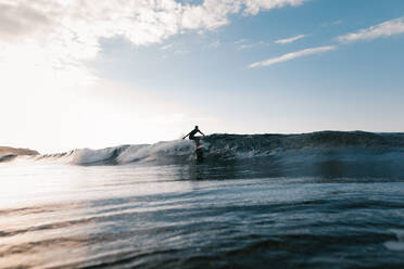 Anonymer männlicher Surfer auf einem Surfbrett bei der Ausübung eines Extremsports auf einer Meereswelle unter bewölktem Himmel - ADSF26005