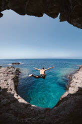 Blick durch ein Höhlenloch auf einen unerkennbaren Mann, der über den endlosen Ozean springt - ADSF26018