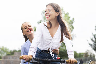 Glückliche Frau, die hinter ihrer Freundin sitzt und Fahrrad fährt - SGF02841