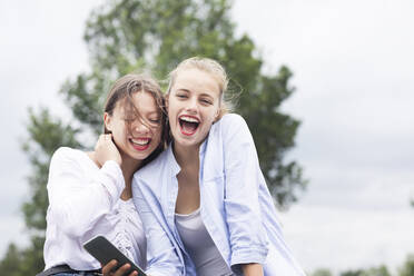 Freundinnen lachen, während sie ihr Smartphone in der Natur halten - SGF02858