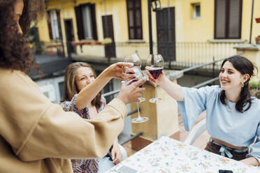 Freundinnen stoßen mit Weingläsern an, während sie auf der Terrasse sitzen - MEUF03438