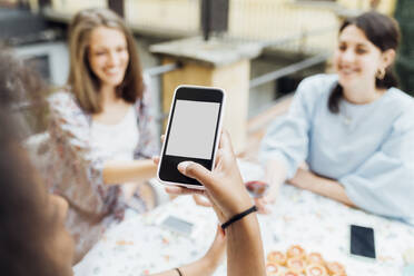 Woman using mobile phone while friends sitting at table in background - MEUF03439