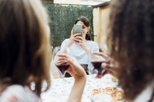 Frau, die ihre Freunde mit dem Smartphone fotografiert, während sie am Tisch sitzt - MEUF03444