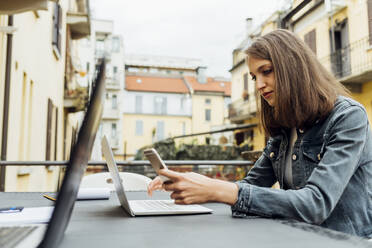 Freiberuflerin mit Laptop und Mobiltelefon, am Tisch sitzend - MEUF03469