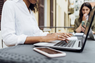 Businesswoman using laptop with colleague in background at terrace - MEUF03470