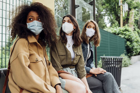 Young women with protective face mask sitting at bus stop - MEUF03498