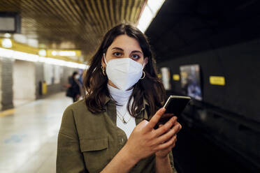 Woman with face mask and mobile phone standing in underground - MEUF03521