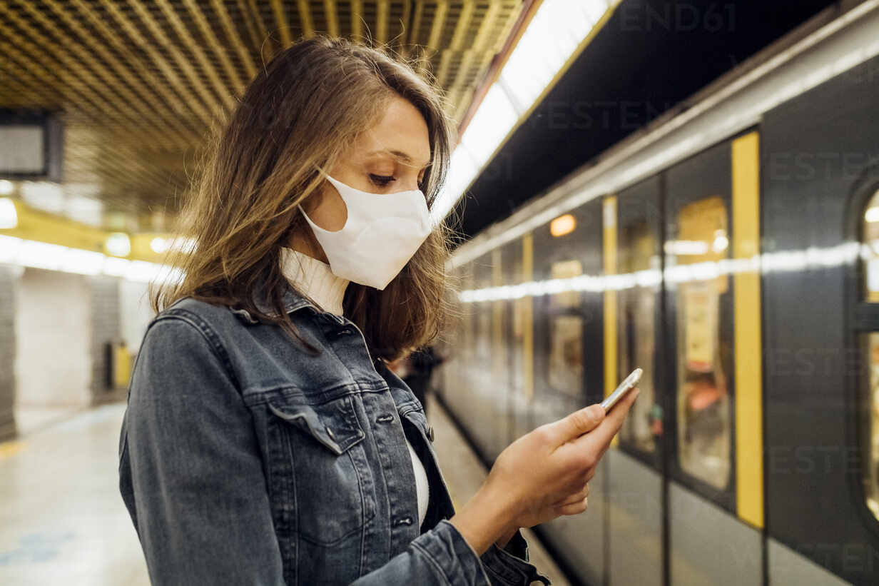 Woman with face mask using mobile phone while standing in subway stock photo