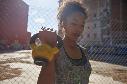 Weibliche Athletin, die an einem sonnigen Tag vor einem Zaun mit einer Kettlebell trainiert - PACF00215