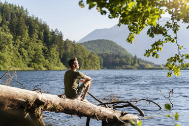 Man looking at view while siting on fallen tree at lake - DIGF16086