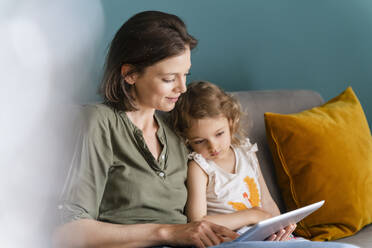 Mother using digital tablet while sitting with daughter at home - DIGF16114