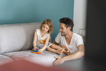 Tochter spielt mit einem Puzzle, während sie neben ihrem Vater im Wohnzimmer sitzt - DIGF16119