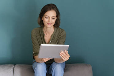 Smiling woman using digital tablet while sitting on sofa - DIGF16121