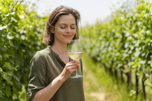 Smiling woman smelling wine while standing at vineyard - DIGF16131