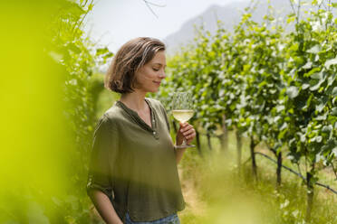 Lächelnde Frau mit Weinglas in der Hand in einem Weinberg stehend - DIGF16138