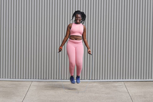 Cheerful woman skipping in front of corrugated wall - AODF00552