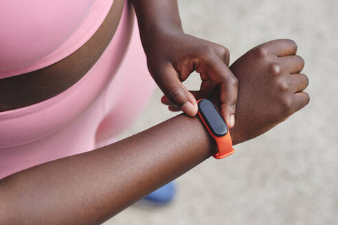 Woman checking time on smart watch while standing on footpath - AODF00554