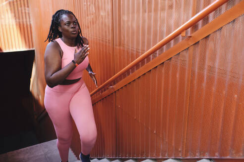 Plus size woman in sports clothing running on staircase - AODF00559