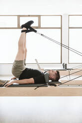 Man stretching legs through cables on pilates machine in exercise room  stock photo