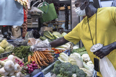 Junger Mann mit Gesichtsmaske kauft Gemüse auf dem Markt - JPTF00869