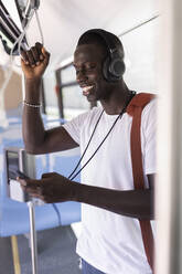 Mann mit Kopfhörern und Umhängetasche benutzt Smartphone im Bus - JPTF00875