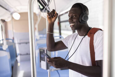 Junger männlicher Berufstätiger mit Kopfhörern und Mobiltelefon im Bus - JPTF00876