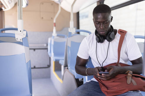 Male commuter using mobile phone while sitting in bus - JPTF00877