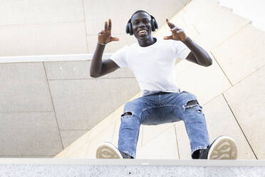 Smiling male professional with headphones dancing while standing at edge of wall - JPTF00881