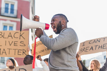 Seitenansicht eines männlichen Afroamerikaners, der während des Black-Lives-Matter-Protests in der Stadt in eine Menge multiethnischer Demonstranten schreit - ADSF26087