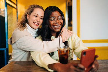 Erfreut multirassischen weiblichen besten Freunde umarmen in Café und Aufnahme selbst Schuss auf Smartphone während genießen Wochenende zusammen - ADSF26125