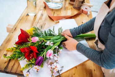 Von oben abgeschnitten unerkennbar weiblichen Florist in Freizeitkleidung und Schürze arrangieren eleganten Strauß von sortierten Blumen im Laden - ADSF26155