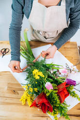 Von oben abgeschnitten unerkennbar weiblichen Florist in Freizeitkleidung und Schürze arrangieren eleganten Strauß von sortierten Blumen im Laden - ADSF26156