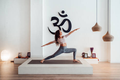 Anmutige junge Frau steht in Virabhadrasana und übt Yoga auf der Matte im Studio - ADSF26159