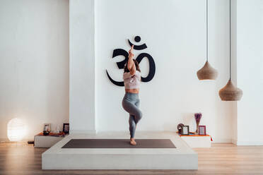 Side view of anonymous flexible women in active wear performing Downward  Facing Dog yoga position in light studio stock photo