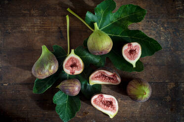 Top view of whole and cut figs with juicy pulp on green foliage with veins on wooden surface - ADSF26215