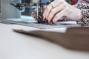 Crop female artisan using sewing machine while creating upholstery for motorbike seat in workshop - ADSF26240