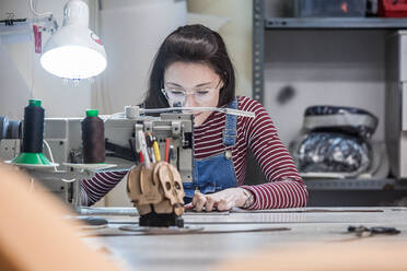 Fokussierte Kunsthandwerkerin bei der Arbeit an der Nähmaschine, während sie in der Werkstatt ein Polster für einen Motorradsitz herstellt - ADSF26241