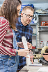 Seitenansicht von zwei kreativen Handwerkern, die an einer Werkbank mit Papierskizzen in einer Werkstatt für die Herstellung von Motorradsitzpolstern stehen - ADSF26246