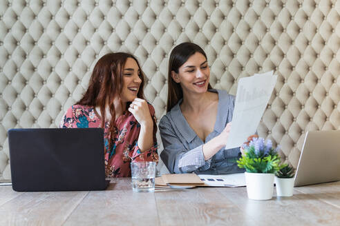 Concentrated young female colleagues in casual clothes working on netbooks and doing paperwork while sitting at desk in light office - ADSF26255