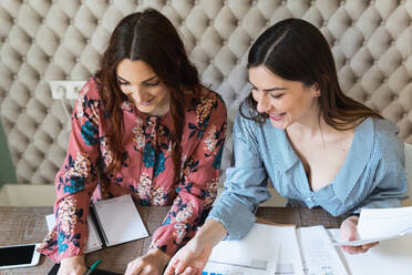 From above crop concentrated female coworkers gathering at desk with laptops and analyzing diagrams while working together in modern workspace - ADSF26258