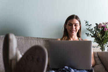 Zufriedene Freundinnen surfen im Internet auf einem Netbook, während sie auf dem Sofa im Haus sitzen - ADSF26303