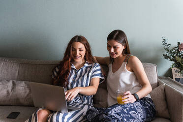 Inhalt beste Freundinnen mit Getränk surfen im Internet auf Netbook beim Sitzen auf Sofa im Haus - ADSF26304