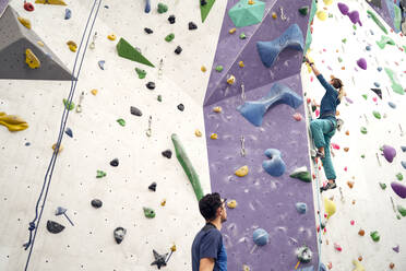 From below of brave female athlete climbing artificial wall in bouldering center under supervision of professional instructor - ADSF26332