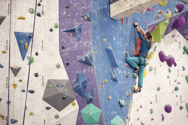 Seitenansicht einer starken Frau im Sicherheitsgurt beim Klettern an der Wand während des Trainings in einer Boulderhalle - ADSF26334