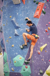 Rückenansicht eines männlichen Bergsteigers in einem Klettergurt, der eine künstliche Wand im Bouldering Center erklimmt - ADSF26339